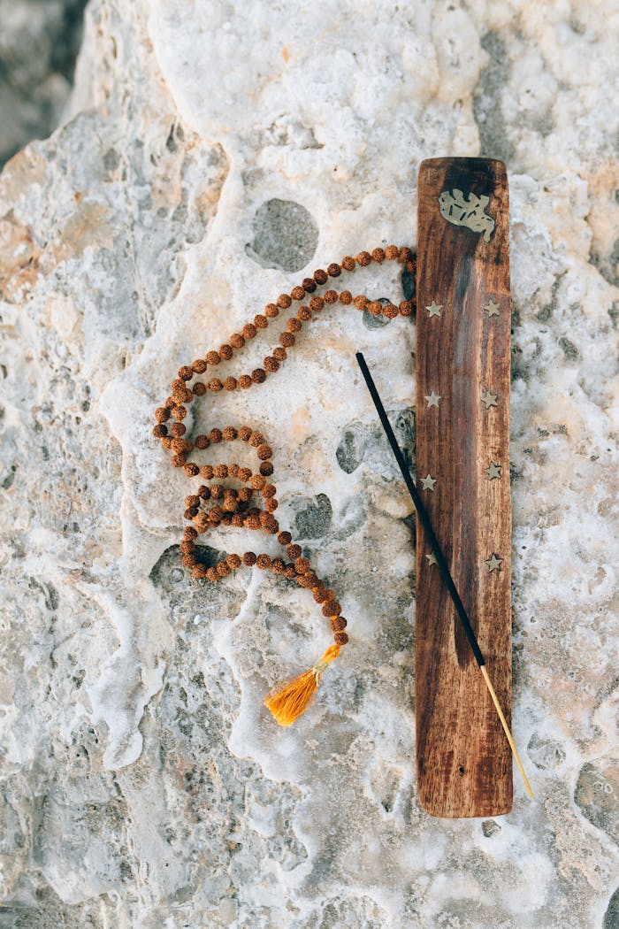 Top view of incense holder and mala beads on textured stone, promoting calm.